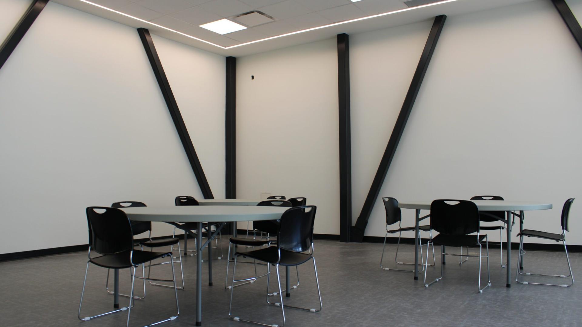 Empty room with tables and chairs, light walls, and diagonal supports.
