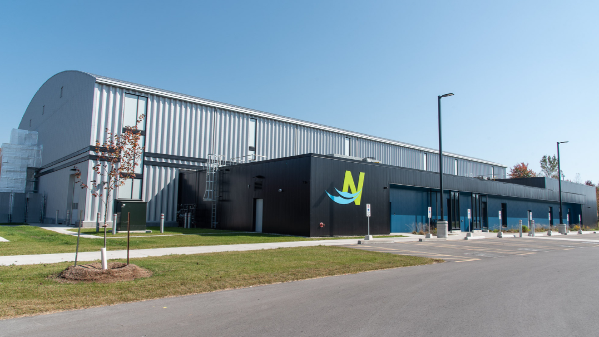 Industrial building with a logo, surrounded by grass and a clear sky.