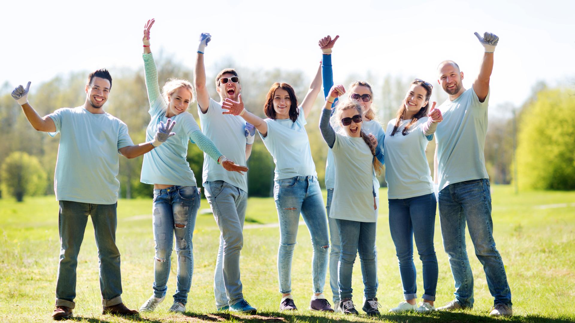 Group of people outdoors wearing matching shirts, smiling and raising hands.