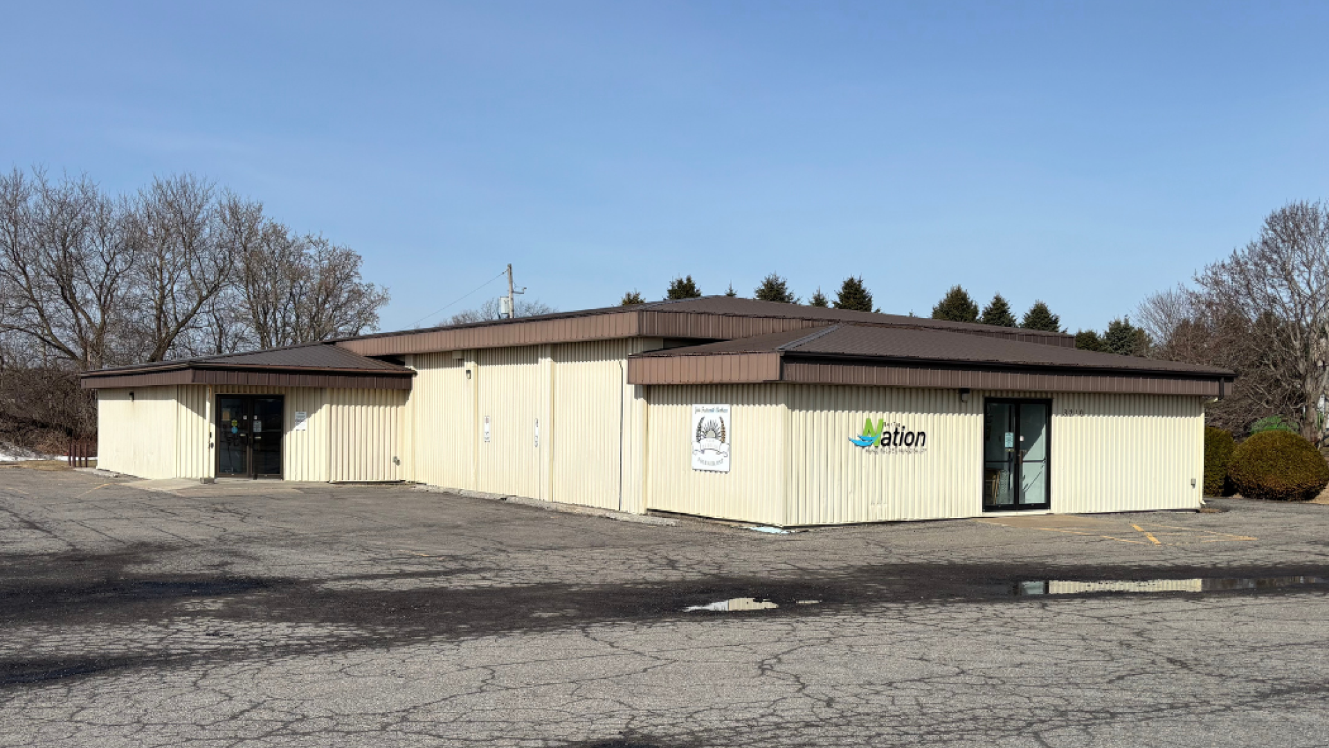 Exterior view of the Fournier Community Hall, showing a single-storey beige building with a brown roof, municipal signage, and an empty paved parking lot in front.