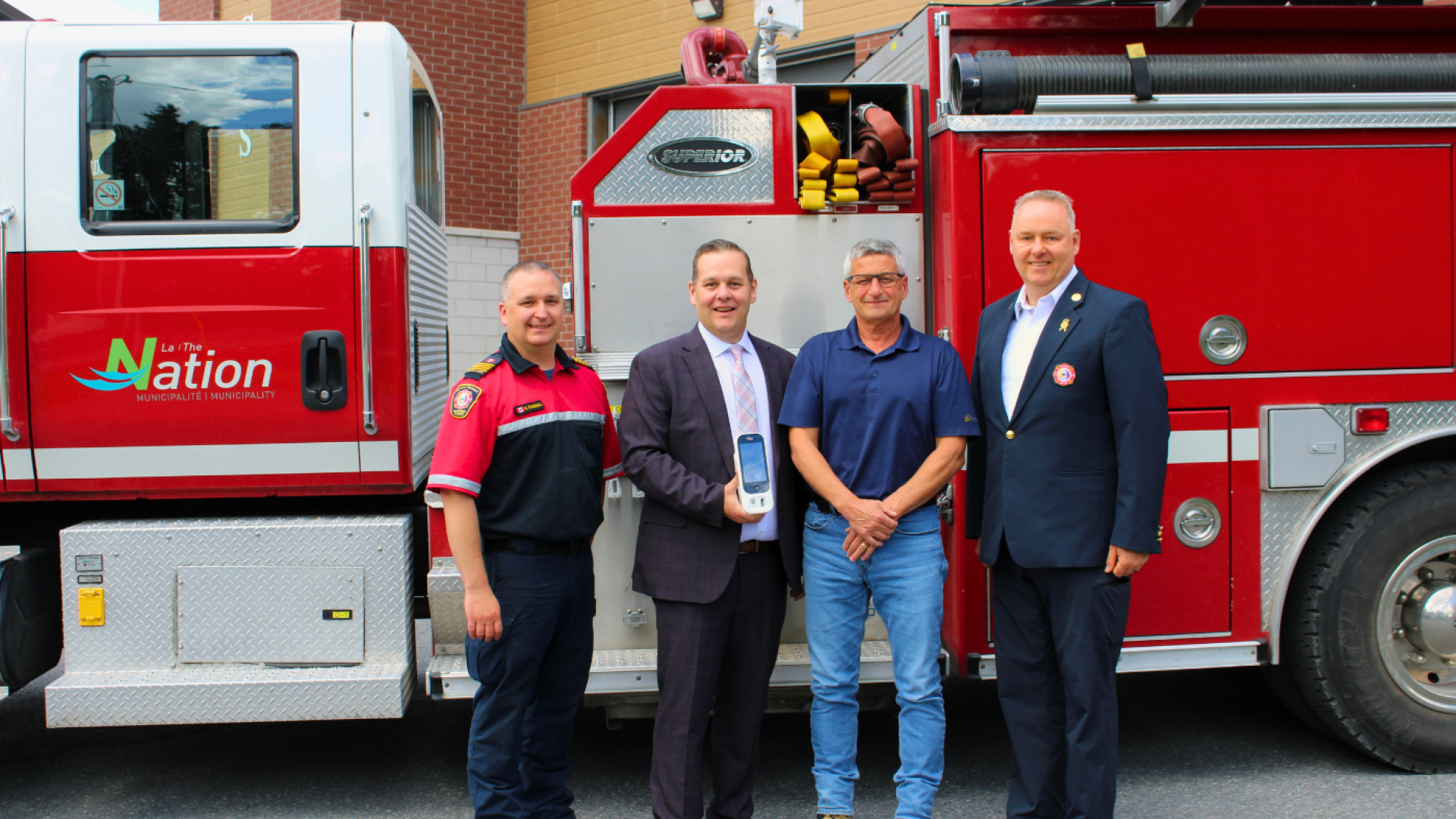 Representatives from The Nation Municipality, The Nation Fire Department, and Enbridge Gas stand in front of a fire truck while displaying a new carbon monoxide monitoring device purchased through Enbridge Gas's Fueling Futures Grant program.