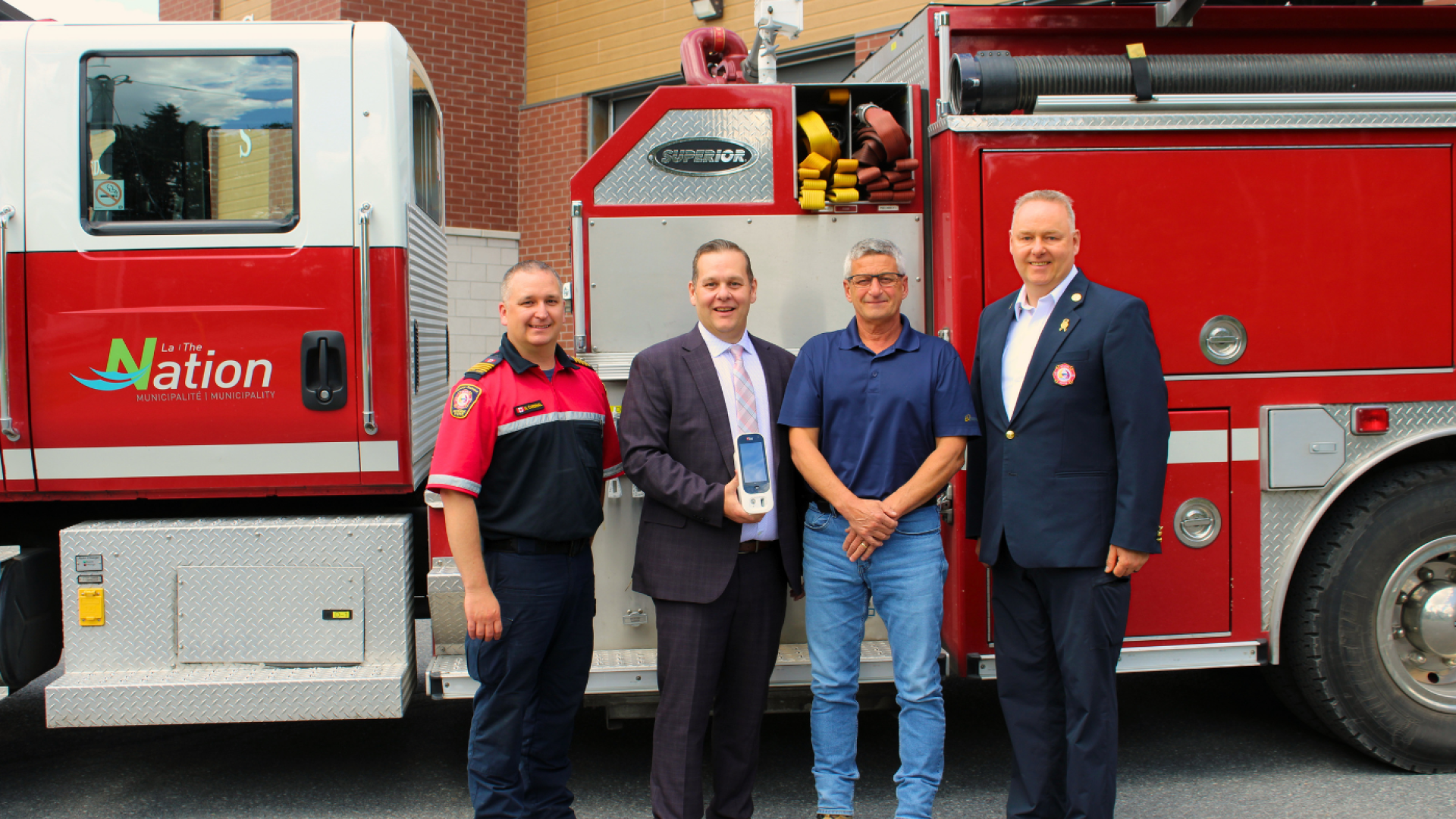 Representatives from The Nation Municipality, The Nation Fire Department, and Enbridge Gas stand in front of a fire truck while displaying a new carbon monoxide monitoring device purchased through Enbridge Gas's Fueling Futures Grant program.