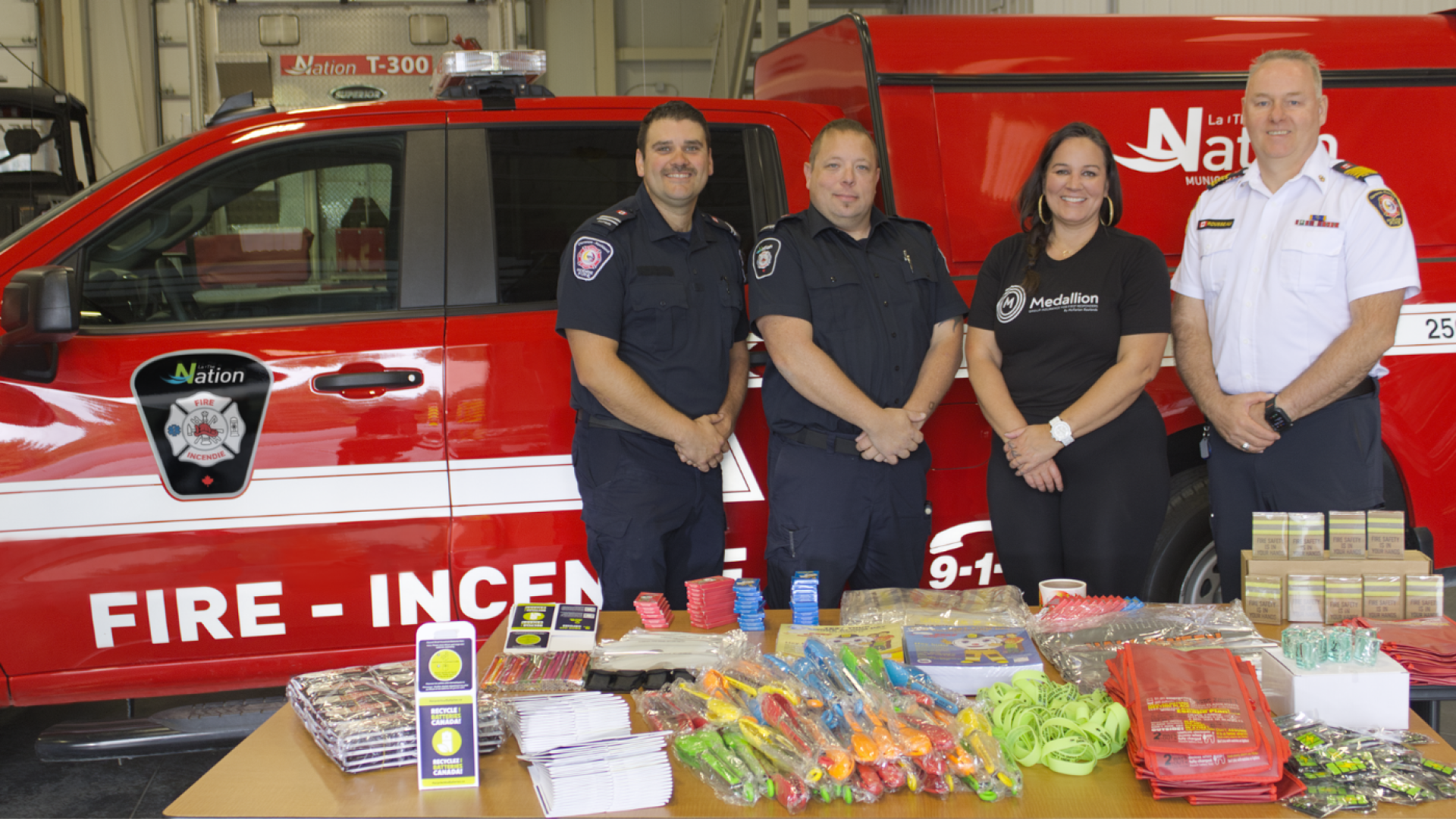  Four people stand in front of The Nation Fire Department vehicles and a table of fire prevention education materials.