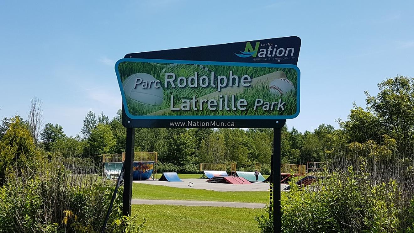 Rodolphe Latreille Park entrance sign with greenery and clear sky.
