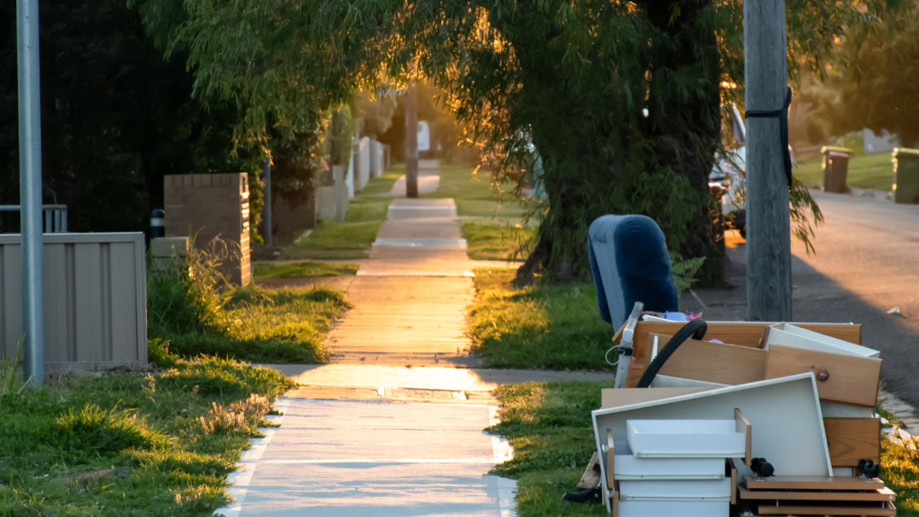 Large household items such as furniture and drawers placed at the curbside along a residential sidewalk for large item collection.