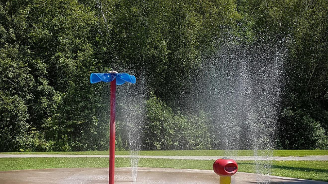 Two small water spraying towers in a splash pad with tall trees in the background
