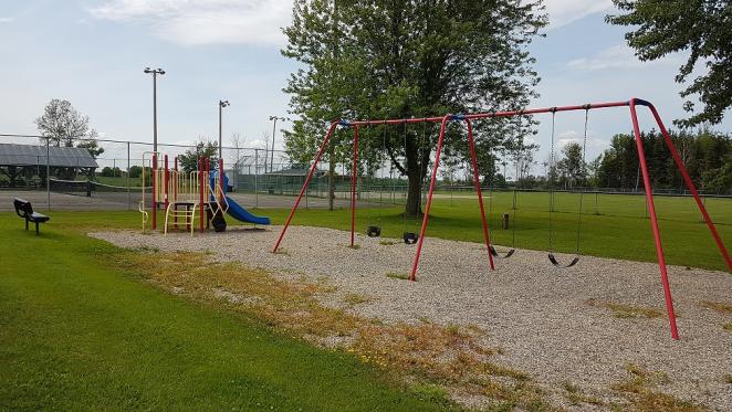 Playground with swings and a slide, surrounded by grass and trees.