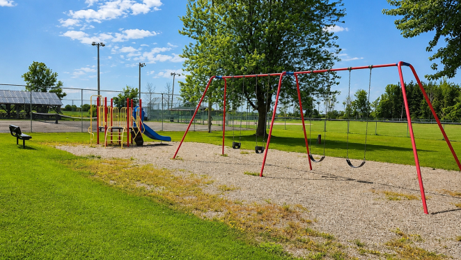 Playground with swings and a slide, surrounded by grass and trees.