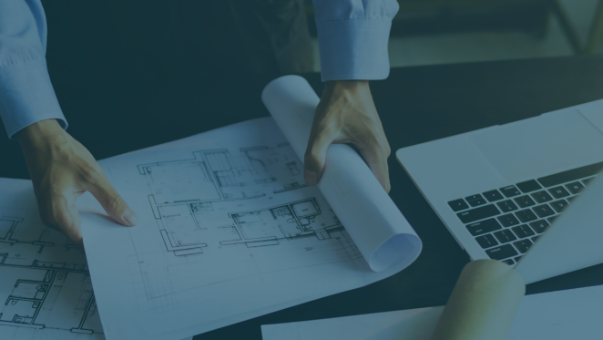 Person reviews building plans, with a laptop nearby