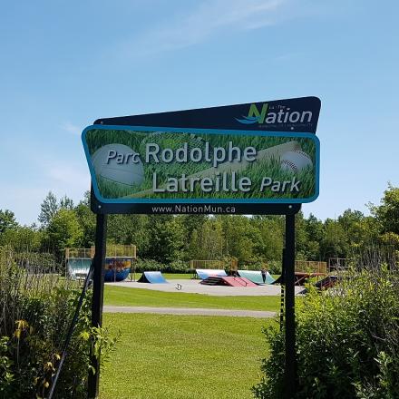 Rodolphe Latreille Park entrance sign with greenery and clear sky.