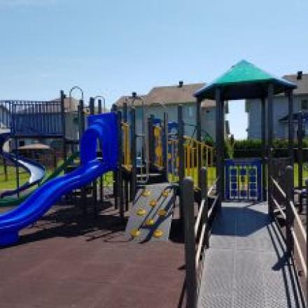 Playground with blue slides, climbing structures, and a canopy, surrounded by houses.