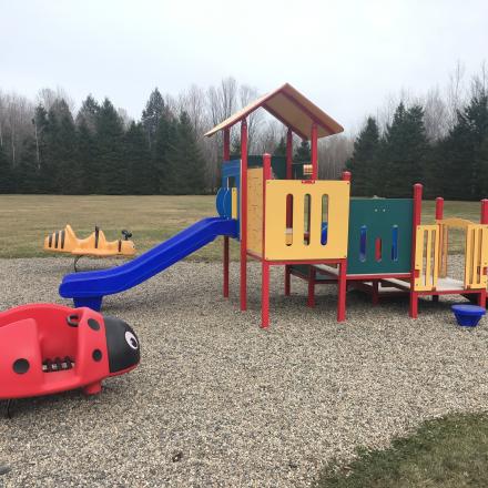 Playground with slides, climbing structure, and a ladybug spring rider on gravel.