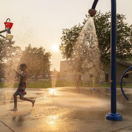 Children playing in a splash pad at sunset, water jets spraying around them.