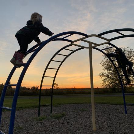 Children climbing a dome-shaped playground structure at sunset.