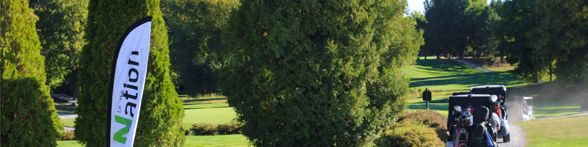 Golf carts heading out to the golf course on a gravel trail surrounded by green grass and pine trees