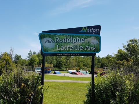 Rodolphe Latreille Park entrance sign with greenery and clear sky.