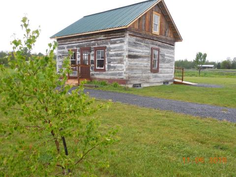 Rustic wooden cabin in grassy field, overcast sky, pathway leading to door.