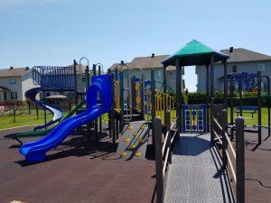 Playground with blue slides, climbing structures, and a canopy, surrounded by houses.
