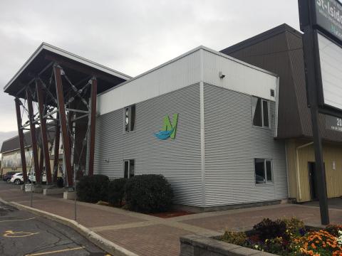 Modern building with a slanted roof, silver siding, and a green-blue logo. Overcast sky.