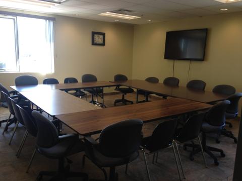 Empty conference room with U-shaped table, chairs, and a wall-mounted TV.