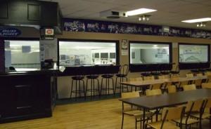 Cafeteria with tables, chairs, counter, and large windows to kitchen.