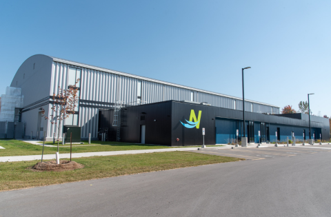 Industrial building with a logo, surrounded by grass and a clear sky.