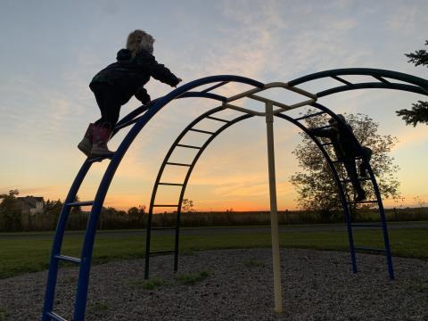 Children climbing a dome-shaped playground structure at sunset.