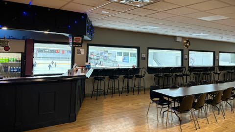 St-Isidore Arena Sports Bar featuring tables, seating, a service counter, and large windows with views of the arena.