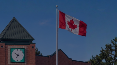 Canadian Flag on blue sky background featuring the top of the Town Hall building.